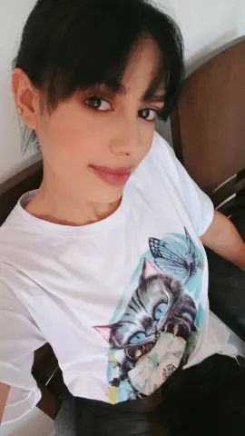 Young woman with dark hair wearing a white graphic cat t-shirt in a relaxed indoor setting.