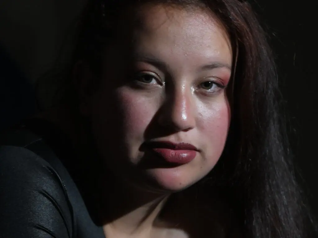 Close-up portrait of a woman with dramatic lighting and soft makeup in a moody, dark setting.