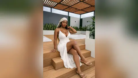 Elegant woman in a white summer maxi dress sitting on wooden stairs by a luxury rooftop pool.