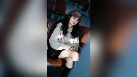 Young woman in a white hoodie and black shorts sitting relaxed in a modern lounge setting.