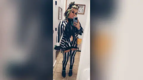 Woman in edgy black and white striped grunge outfit taking a mirror selfie in a modern room.
