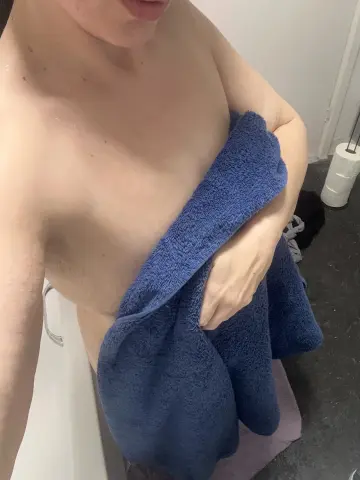 A shirtless man wrapped in a blue towel in a bright bathroom setting.