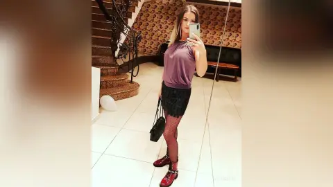 Woman in a mauve halter top and black skirt taking a mirror selfie in a modern home hallway.