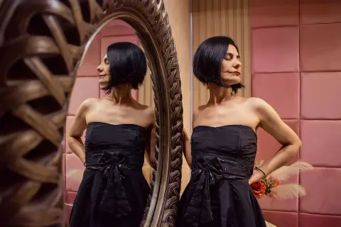 Elegant woman in a black strapless cocktail dress posing confidently in front of a vintage mirror.
