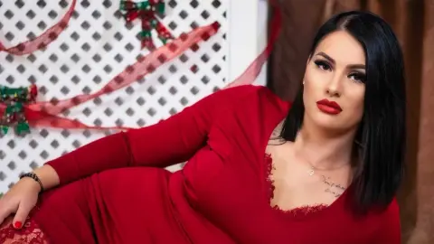 Glamorous woman in a red lace dress posing against a festive white lattice background.