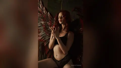 RubyAttwood poses with eyes closed, wearing black lace panties and a black bra, framed by large red and black feathered wings.