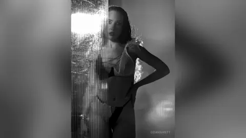 Moody black and white portrait of a woman in a white bikini posing in a reflective, shimmering setting.