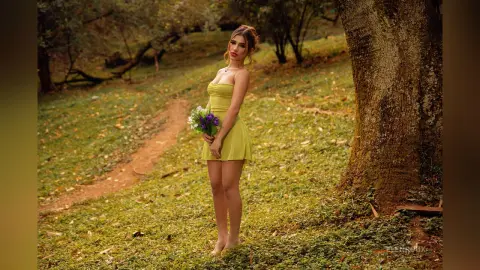 Young woman in a yellow summer dress holding wildflowers in a lush green forest setting.