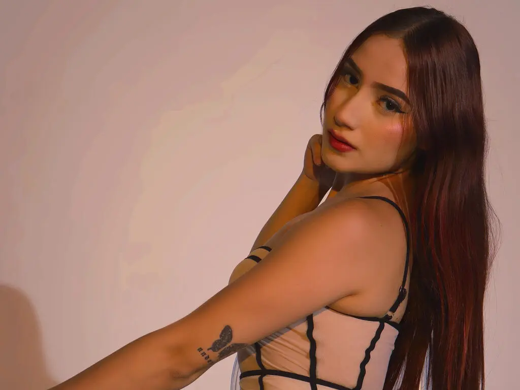 Young woman with long reddish hair wearing a beige corset top against a neutral studio background.