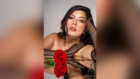 Elegant woman in black sheer gloves holding a red rose in a moody, romantic portrait.