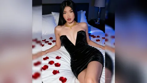 AnastasiaVelo — AnastasiaVelo wears a tight black velvet mini dress while lying on a white bed scattered with red rose petals.
