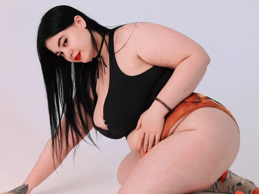 Curvy woman with long black hair in a black halter top and orange shorts posing against a white background.