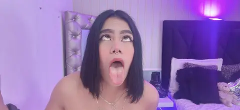 Young woman with dark hair making a funny face in a bedroom with purple ambient lighting.