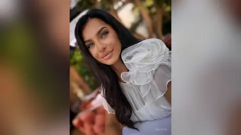 Beautiful woman in a white ruffled blouse smiling outdoors in soft natural lighting.