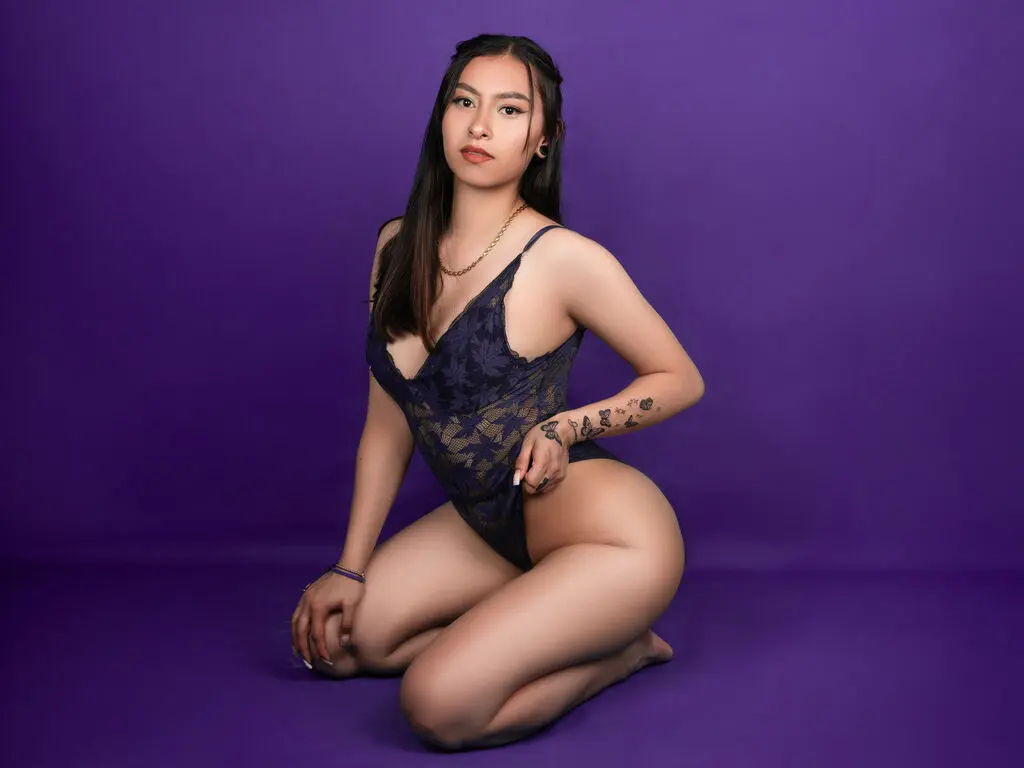 Young woman in a dark navy lace bodysuit posing confidently against a vibrant purple studio background.