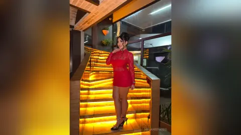Elegant woman in a red lace cocktail dress posing on glowing modern stairs in a luxury interior setting.