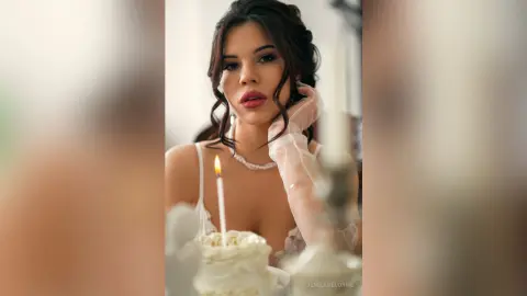 Elegant woman in white lace outfit posing with a lit birthday candle for a romantic, dreamy celebration.