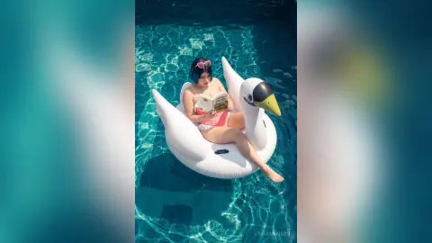 Young woman in pink bikini relaxing on a white swan floatie in a sunny swimming pool.