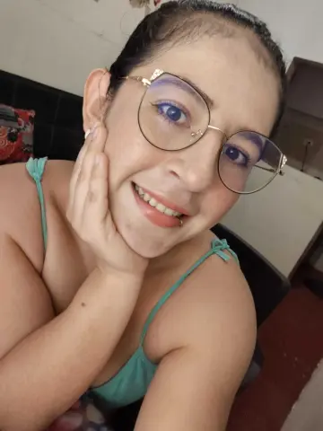 Smiling woman with glasses and mint green camisole in a cozy indoor setting.