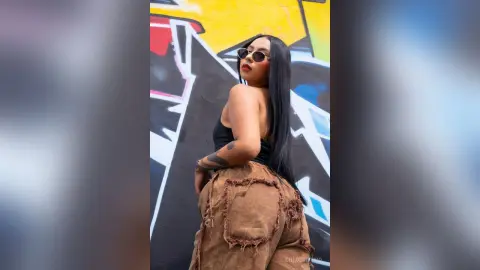 ChloeRiveiro — Stylish woman in black tank top and brown fringed denim posing against a colorful urban graffiti wall.