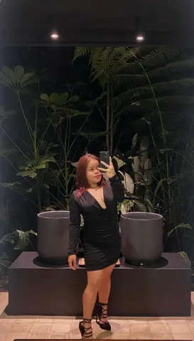 Woman in a sleek black long-sleeve mini dress posing in a lush tropical garden at night.
