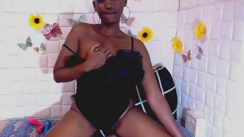 Young woman in a black lace bodysuit sitting in a room decorated with sunflowers and butterfly wall art.