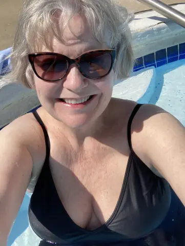 Smiling woman in black bikini and sunglasses relaxing in a sunny swimming pool.