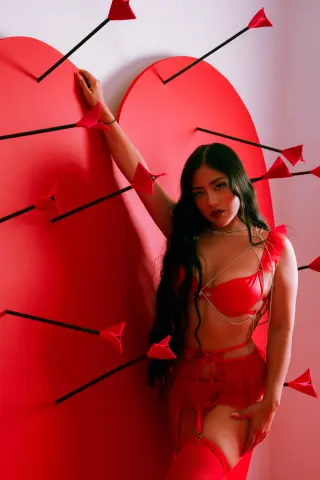 Nicol_Pierce poses in red lingerie and stockings against a large red heart with arrows.