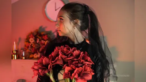 Moody portrait of a woman in a black veil holding a bouquet of deep red roses in warm lighting.