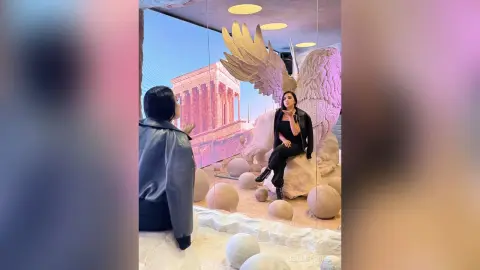 Woman in black outfit admiring a large golden angel wing sculpture in a modern museum setting.