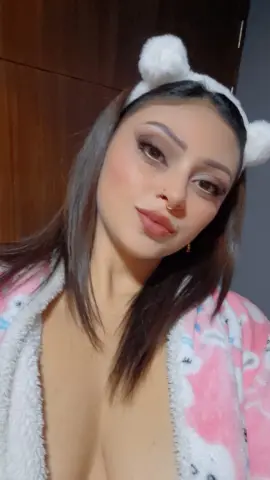 Young woman in a pink fuzzy robe and white bear ear headband posing in a cozy indoor setting.