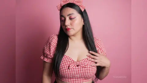 Young woman in red gingham crop top and bow headband posing against a pink background with a soft aesthetic.