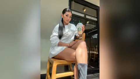 Stylish woman in a white oversized shirt sitting at a cafe with a Starbucks drink, enjoying a sunny afternoon.