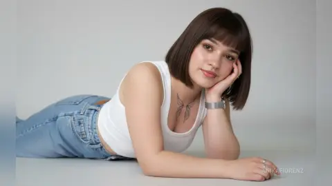 Young woman with short brown hair in a white tank top and blue jeans lying on a white floor with a calm mood.