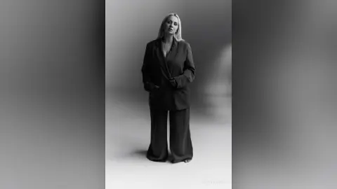 Elegant woman in a black oversized blazer and wide-leg trousers posing in a minimalist studio setting.