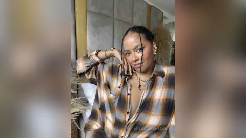 Smiling woman in a plaid flannel shirt relaxing in a cozy bedroom setting.