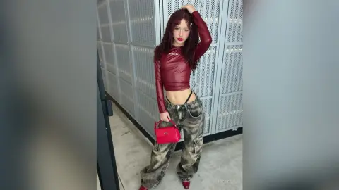 Stylish woman in a red long-sleeve crop top and baggy grey jeans posing confidently in a modern industrial setting.