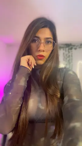 MadelineBrooks wears glasses and a sheer grey long-sleeve top while posing with her hand to her chin.