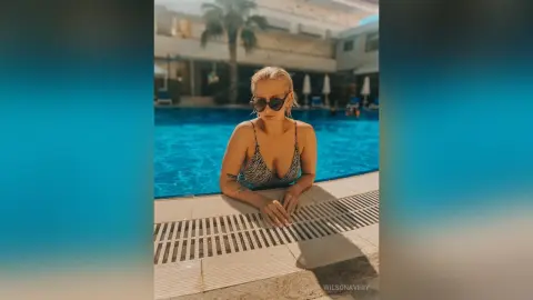 Blonde woman in a zebra print bikini relaxing by a sunny outdoor swimming pool.