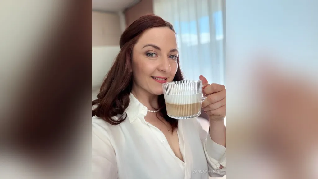 VarvaraMori — VarvaraMori smiles while holding a glass of coffee in a white button-down shirt.