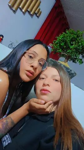 Two young women with long hair posing closely for a selfie in a cozy indoor setting.