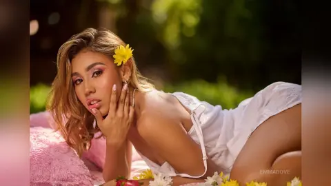 Beautiful blonde woman in a white summer outfit relaxing on a pink towel in a sunny garden setting.