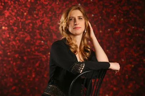Elegant woman in a black lace outfit sitting against a romantic red floral background.