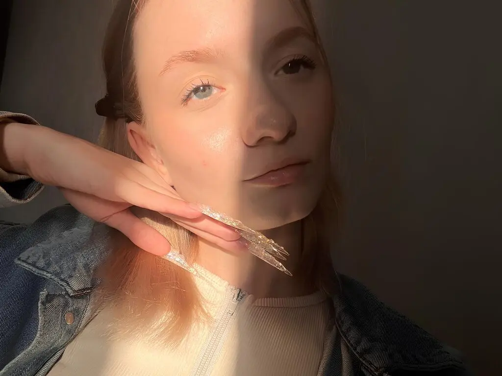 Young woman with long manicured nails wearing a denim jacket in warm sunlight.