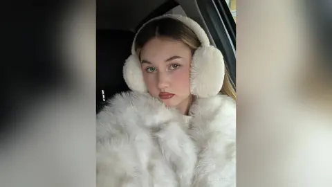 Young woman in a cozy white faux fur coat and fluffy earmuffs sitting in a car with a soft aesthetic mood.