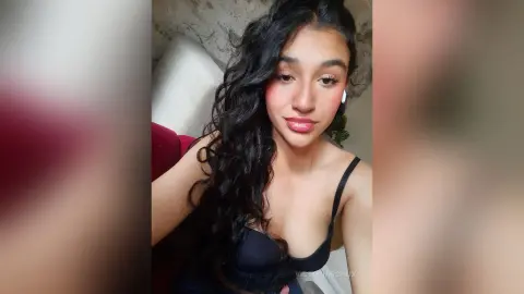 Young woman with long wavy hair wearing a black camisole in a cozy indoor setting with a soft, natural mood.