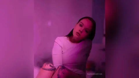 Young woman in a white top posing in moody pink lighting for a dreamy aesthetic portrait.