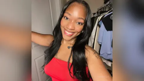Smiling Black woman in a red top posing in a bright room with clothing racks in the background.