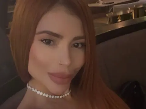 Glamorous woman with long auburn hair wearing a sparkling diamond choker in a dimly lit lounge setting.