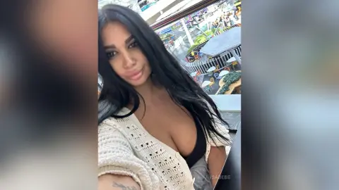 Smiling brunette woman in a white knit cardigan relaxing outdoors on a sunny day.